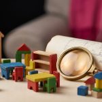 Nursery Furniture Case Study - Professional 16:9 hero banner. Ultra high resolution. A macro shot focusing on a miniature, perfectly arranged nursery classroom scene, built from colourful, multi-functional wooden blocks and small, child-safe furniture pieces. A miniature magnifying glass, partially reflecting a soft glow of #737373 light, rests on a tiny blueprint of a nursery layout, symbolising meticulous planning and expert analysis. The background features blurred elements of #E2087E and #000000, suggesting a vibrant yet organised educational environment. The scene evokes a sense of thoughtful design and successful transformation. Style: Fine art still life photography. Avoid: Groups around holographic tables, generic tech aesthetics, text overlays, cold blue tones, stock photo clichés.