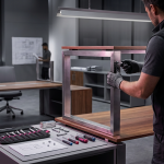 office furniture installation - Professional 16:9 hero banner. Ultra high resolution. A skilled technician in professional work attire, seen from behind, meticulously tightening a bolt on a sleek, modern office desk. The scene is set in a newly furnished, expansive office space, with other partially assembled furniture in the background, hinting at a large-scale project. Dramatic, focused lighting from a #737373 (grey) source highlights the precision of the work, casting subtle magenta (#E2087E) and black (#000000) shadows that define the clean lines of the furniture. The atmosphere is one of efficiency and expertise, reflecting the brand's authoritative and customer-centric voice. The composition emphasizes the 'seamless setup' concept, with tools and components organised neatly, signifying organised project management. Style: Editorial photography, with a focus on detail and professionalism. Avoid: Groups around holographic tables, generic tech aesthetics, text overlays, cold blue tones, stock photo clichés.