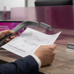 Office Furniture Myths - Professional 16:9 hero banner. Ultra high resolution. A discerning procurement professional's hands, in a modern, well-lit UK office setting, carefully examining a broken, flimsy office chair component, contrasting it with a blueprint or diagram of a robust, BS-compliant furniture joint. The scene is bathed in a subtle accent glow of #737373, with hints of #E2087E in background elements like a desk partition or digital display. The overall mood is authoritative and analytical. Style: Editorial photography, with a focus on detail and texture. Avoid: Groups around holographic tables, generic tech aesthetics, text overlays, cold blue tones, stock photo clichés.