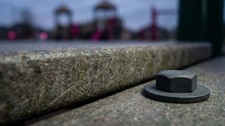 Outdoor School Furniture - Professional 16:9 hero banner. Ultra high resolution. A macro shot focusing on the intricate, weather-worn yet resilient surface of a recycled plastic (HDPE) plank, contrasted with a subtly textured powder-coated steel component, both illuminated by a precise (#737373) accent glow highlighting their durability. A faint, almost artistic hint of (#E2087E) suggests the vibrant life of a school playground in the background, out of focus. The composition emphasizes strength and longevity, with a subtle nod to sustainability. Style: Editorial still life photography, rich textures, shallow depth of field. Avoid: Generic school children, pristine new furniture, overtly digital interfaces.