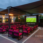 Pub Outdoor Space - Professional 16:9 hero banner. Ultra high resolution. A meticulously organised pub beer garden, seen from an elevated perspective, with distinct 'zones' clearly delineated by subtle, glowing lines in #737373. Modern, commercial-grade outdoor furniture in shades of #000000 and #E2087E is strategically placed, leading towards a large outdoor screen showing a football match. The scene pulses with a confident, authoritative atmosphere, suggesting expert planning and profitability. Overhead, a retractable awning is partially extended, and strategically placed commercial patio heaters emit a soft, warm glow. Style: Architectural photography with a clean, editorial finish. Avoid: Groups around holographic tables, generic tech aesthetics, text overlays, cold blue tones, stock photo clichés.