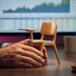 Cost-Saving Classroom Furniture - Professional 16:9 hero banner. Ultra high resolution. A pair of expert hands, belonging to a UK school business manager, carefully examining a miniature, durable classroom chair model. The chair is made from high-quality, compliant materials. The hands are resting on a desk with a blurred financial graph in the background, subtly indicating budget management. Accent lighting in #737373 casts a focused glow on the chair, with a hint of #E2087E in the background, symbolising smart investment. Style: Editorial photography with a shallow depth of field. Avoid: Groups around holographic tables, generic tech aesthetics, text overlays, cold blue tones, stock photo clichés.