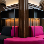 Education Planning Advice - Professional 16:9 hero banner. Ultra high resolution. A close-up, architectural detail shot showcasing the intersection of traditional and modern educational design within a prestigious UK school setting. Focus on a section of a high-ceilinged, well-lit school hallway or library, where classic wooden architectural elements meet sleek, modular, brightly coloured (in #E2087E and #000000) furniture pieces. The scene should convey a sense of purposeful evolution, with a warm, inviting glow from accent lighting in #737373 subtly highlighting the adaptable furniture. The composition should suggest forward-thinking design without being overtly futuristic. Style: Editorial architectural photography. Avoid: Groups around holographic tables, generic tech aesthetics, text overlays, cold blue tones, stock photo clichés.