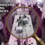 Office Layout Mistakes - Professional 16:9 hero banner. Ultra high resolution. A conceptual yet realistic overhead shot of a modern, slightly disorganised office space in the UK, viewed through a magnifying glass. The magnifying glass highlights a specific 'mistake' – perhaps a cluttered walkway or an isolated desk, while the rest of the office appears blurred but still hints at inefficiencies. The accent glow of #737373 emanates from the magnified area, drawing attention to the problem, with subtle hints of #E2087E in the overall office lighting. The scene conveys a sense of critical analysis and problem identification in a corporate setting. Style: Editorial photography.