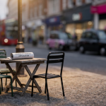 Getting Started - Professional 16:9 hero banner. Ultra high resolution. A close-up, macro shot of a meticulously detailed miniature cafe scene set on a UK pavement. Focus on a tiny, weathered wooden cafe table and two stackable outdoor chairs, with a miniature copy of a 'Pavement Licence Application' document, illuminated by a warm #737373 glow. The background subtly hints at a bustling UK high street, blurred with accents of #E2087E and #000000, suggesting the real-world context. The scene should evoke precision, planning, and expert guidance. Style: Fine art still life photography with a shallow depth of field. Avoid: Groups of people, generic cafe scenes, text overlays, cold blue tones.