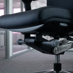 Advanced Ergonomics - Professional 16:9 hero banner. Ultra high resolution. A close-up, architectural detail shot of a sophisticated, high-end ergonomic office chair, focusing on its intricate adjustment mechanisms. The chair is positioned in a sleek, modern UK office interior with subtle light reflections. The shot highlights the precision engineering of the chair's components, with a strong accent glow of #737373 emanating from beneath the seat and along adjustment levers, contrasting with the chair's dark upholstery and the #E2087E subtle backlighting of a distant window. The overall mood is authoritative and technical, showcasing the chair as a piece of advanced engineering. Style: Editorial photography with a focus on product design.