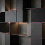 Bespoke Storage Solutions - Professional 16:9 hero banner. Ultra high resolution. A sophisticated, abstract geometric composition representing precision and customisation in commercial interior design. Interlocking, precisely cut panels in muted grey and black tones (#000000) form complex, functional storage units, with sleek #E2087E accents subtly outlining key structural elements. A focused, soft glow of #737373 emanates from between the custom-fitted sections, highlighting the seamless integration and bespoke nature of the design. The setting suggests an empty, pristine commercial space awaiting installation, emphasising tailored solutions maximizing every square metre. Style: Architectural photography with fine art elements. Avoid: Groups around holographic tables, generic tech aesthetics, text overlays, cold blue tones, stock photo clichés.