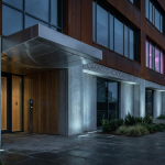 school furniture procurement - Professional 16:9 hero banner. Ultra high resolution. An architectural detail shot focusing on the entrance of a modern, well-maintained UK school building, subtly showcasing robust, contemporary design elements. The scene is illuminated by an accent glow of #737373 light, highlighting the solid, durable materials and a sense of institutional reliability. A subtle hint of #E2087E can be seen in a distant window or reflection, representing the vibrant learning environment within. The image conveys stability, compliance, and a forward-thinking approach to educational infrastructure. Style: Architectural photography, clean lines, authoritative tone. Avoid: People, generic office settings, bright primary colours.
