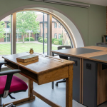 Flexible Learning Furniture - Professional 16:9 hero banner. Ultra high resolution. A visually striking architectural detail within a modern, adaptable UK school classroom, showcasing the seamless blend of traditional and flexible learning furniture. A sturdy, classic wooden student desk with a modern, ergonomic, colourful flexible chair is positioned next to a modular, reconfigurable table. The lighting subtly highlights the innovative elements with a soft #737373 glow, while hints of #E2087E and #000000 are integrated into the furniture's design or background elements. The scene conveys a sense of thoughtful design and future-focused education. Style: Editorial architectural photography. Avoid: Groups around holographic tables, generic tech aesthetics, text overlays, cold blue tones, stock photo clichés.