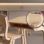 School Furniture Issues - Professional 16:9 hero banner. Ultra high resolution. A meticulously organised school classroom, bathed in a soft, authoritative glow of #737373 from overhead lighting. The scene focuses on a pristine, ergonomic school desk and chair, both certified to BS EN 1729 standards, with subtle structural details highlighted. In the foreground, a magnifying glass hovers over a pristine surface, symbolising inspection and prevention, while in the background, out of focus, blurred outlines of well-maintained school furniture recede into the distance. The overall composition suggests order, durability, and proactive management. Hints of #E2087E subtly define structural elements or a background wall. Style: Precision still life photography with a clean, educational aesthetic. Avoid: Groups around holographic tables, generic tech aesthetics, text overlays, cold blue tones, stock photo clichés.